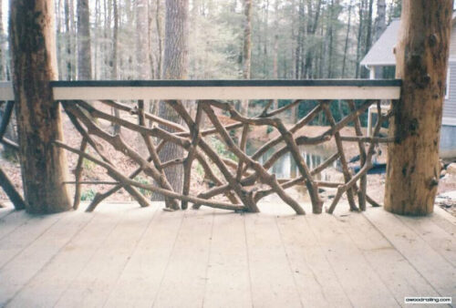 Deck with dense woven twig railing and log posts near forest.
