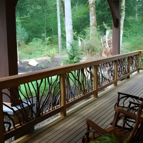 Wooden deck with handcrafted woven branch railing, wooden chairs, and a lush green forest view in the background.