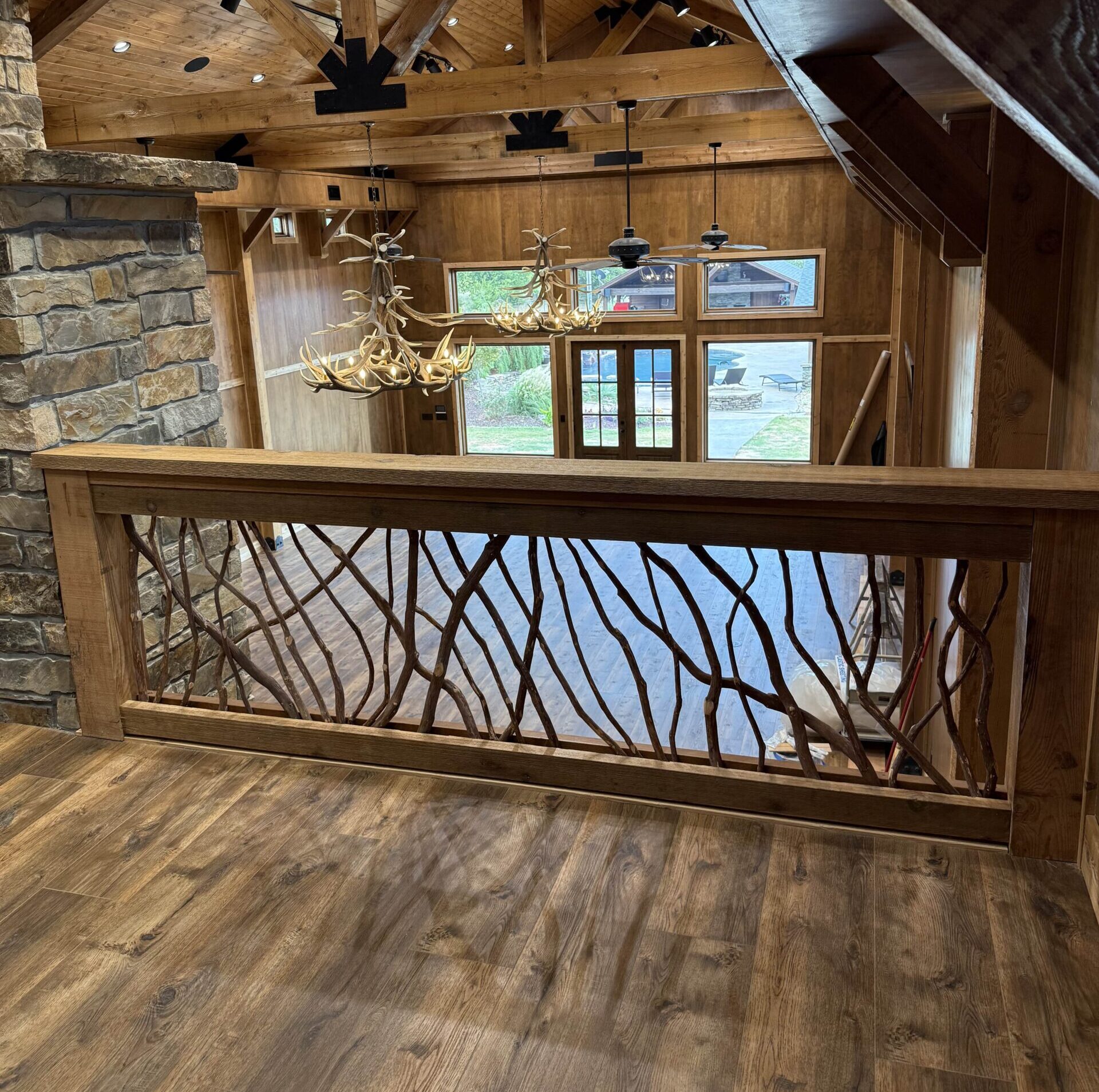 Rustic wooden interior with exposed beams, stone fireplace, antler chandelier, and decorative railing.