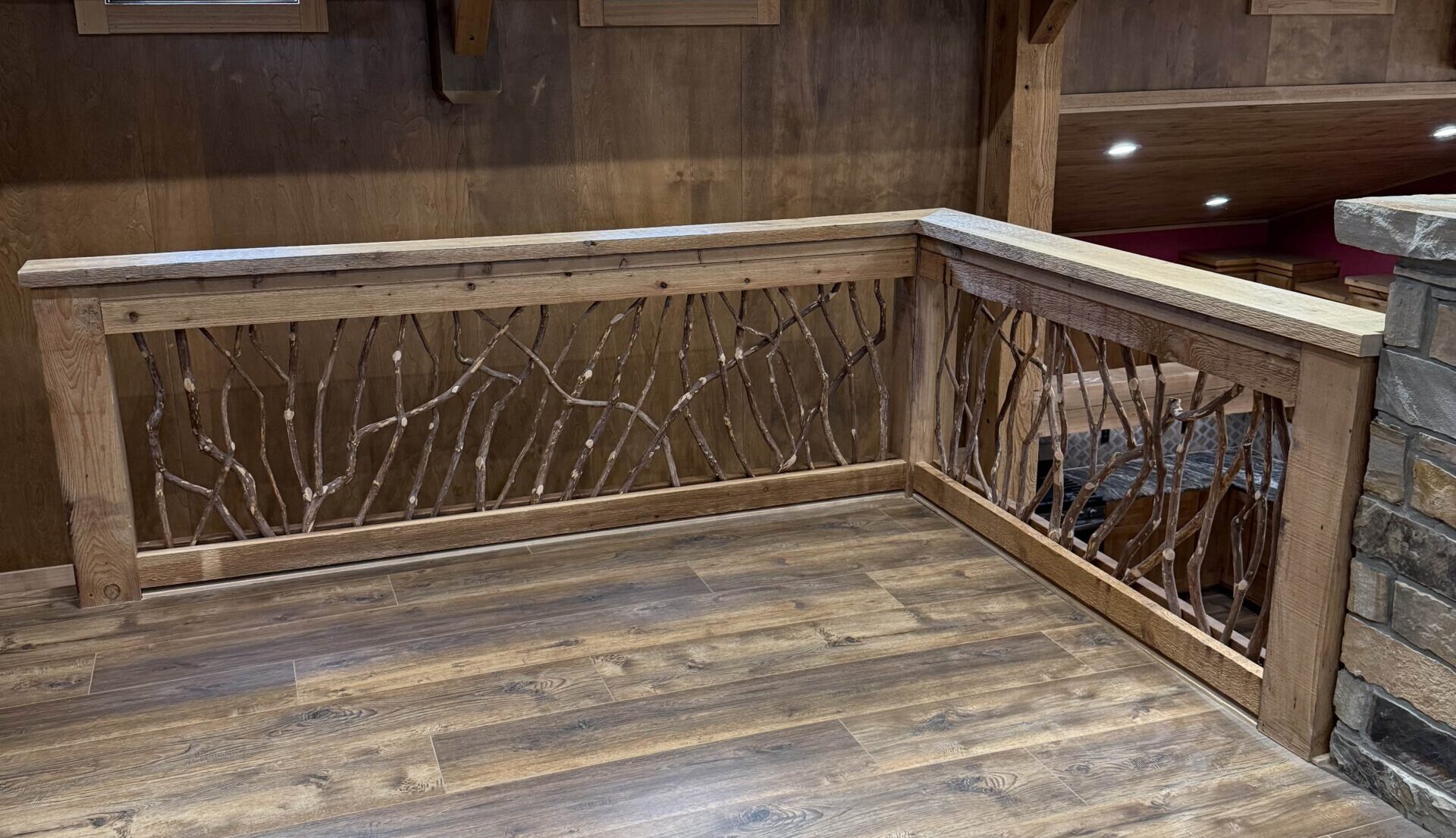 Wooden balcony railing with twig-like design, overlooking a rustic interior with wood floors and walls.