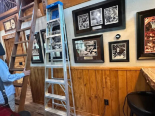 Rustic Cabin Loft with Ladder and Gallery Wall Wooden ladder and metal step ladder beneath a loft with branch railing and framed photos on a wood-paneled wall.