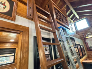 Rustic Loft Ladder with Custom Branch Railing Wooden ladder leading to a loft with branch-style railing in a rustic cabin interior with exposed wood beams.