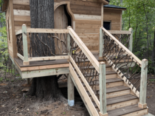 Treehouse Cabin with Branch Railings Wooden treehouse cabin with staircase and woven branch railings built around a large tree.