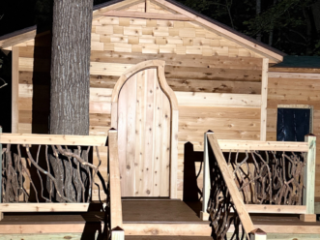 Woodland Cabin with Natural Railing Small wooden cabin with branch-style railing and steps in a wooded area at night.