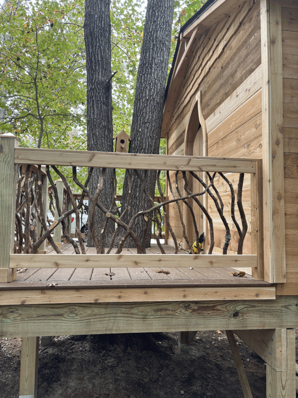 Wooden platform with decorative woven branch railing next to a cabin wall.