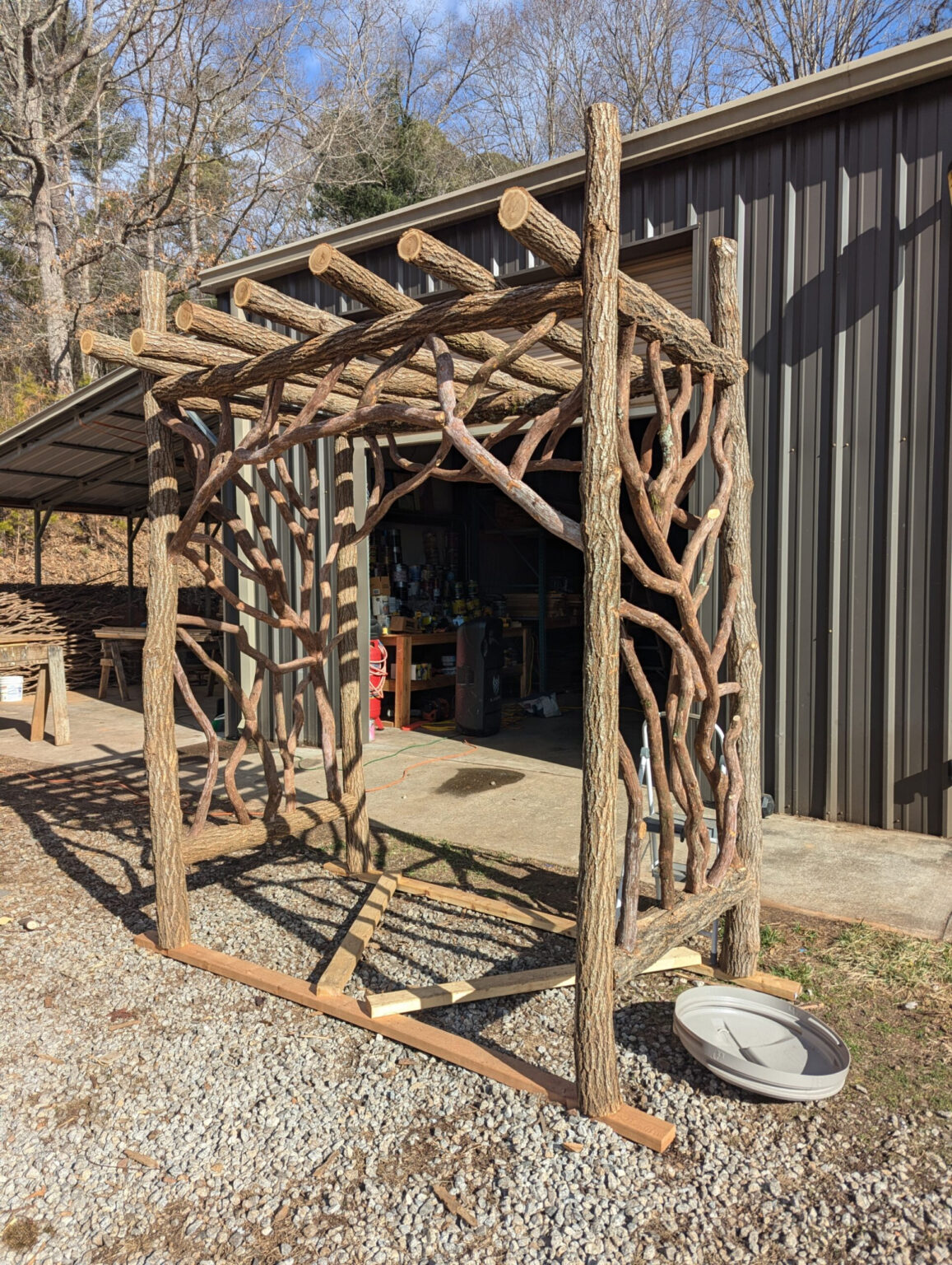 Outdoor pergola frame with woven branch panels and log posts.