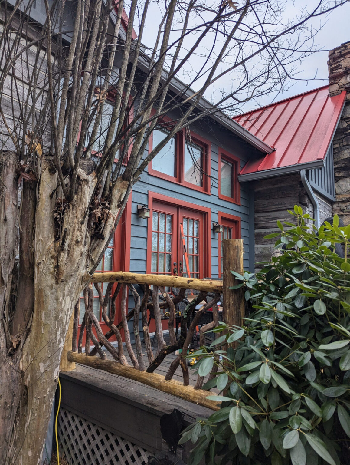 Rustic woven branch railing on a wooden deck in front of a house with red trim and red roof.