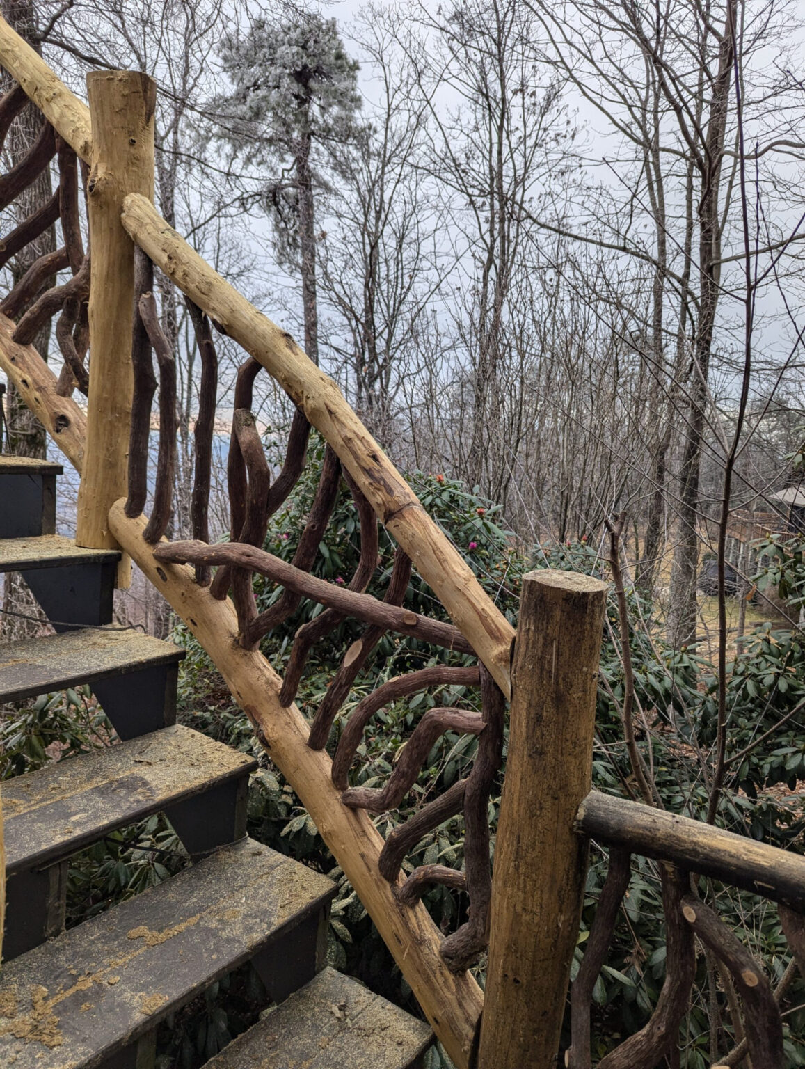 Rustic wooden staircase with woven branch railing in a forest setting.