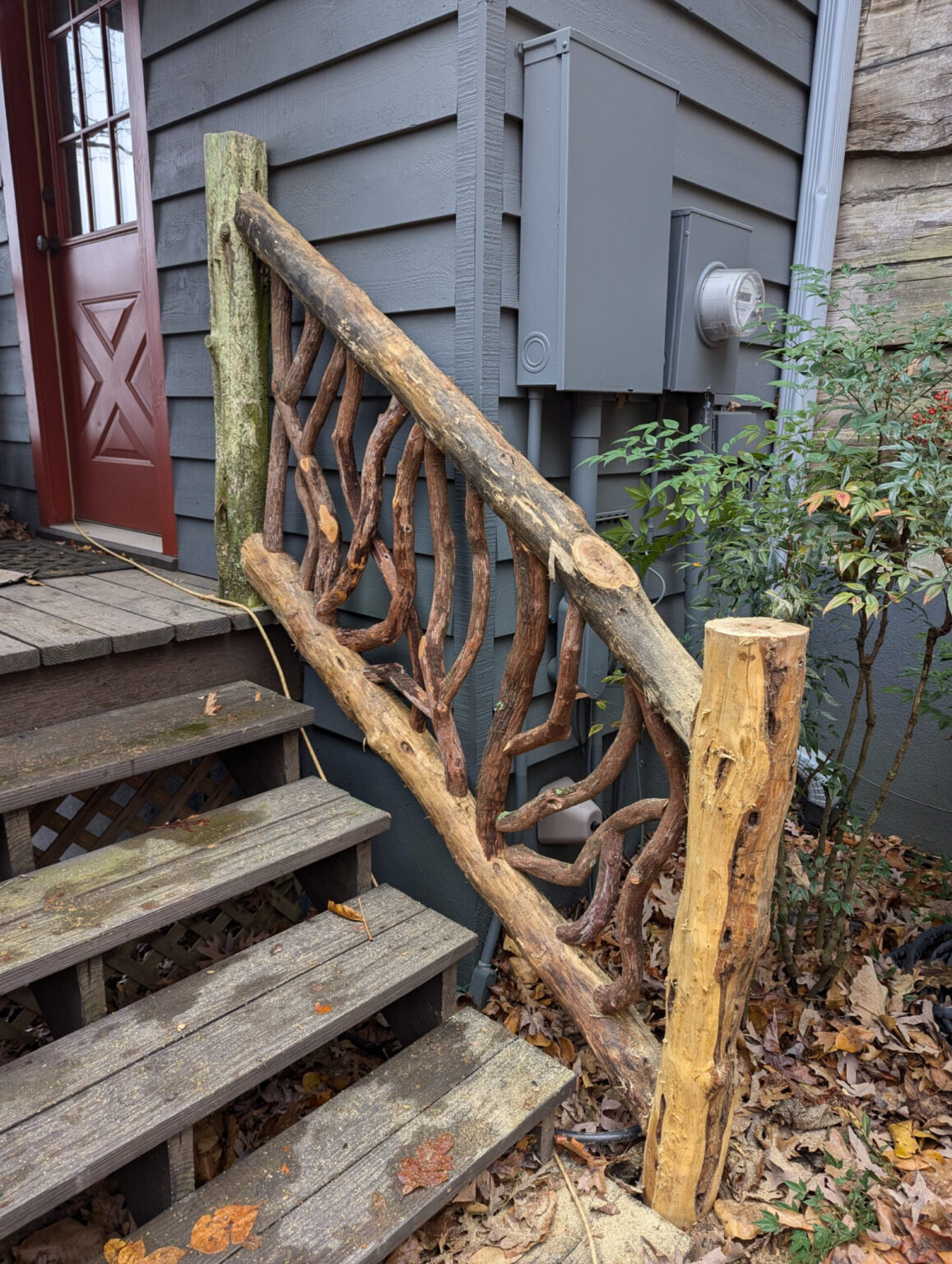 Rustic woven branch railing on wooden stairs next to a house exterior.