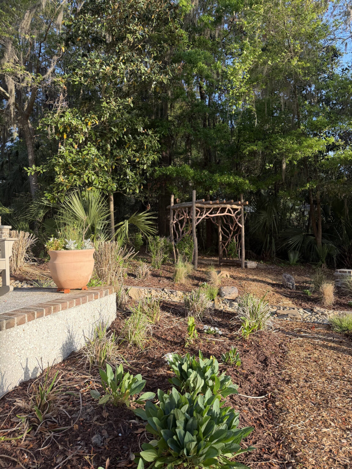 Lanscaping behind home blends with rustic log and branch arbor