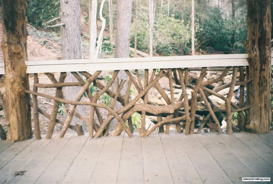 Wooden deck with dense handcrafted woven branch railing made of natural twigs and branches, set against a forest backdrop with tall trees.