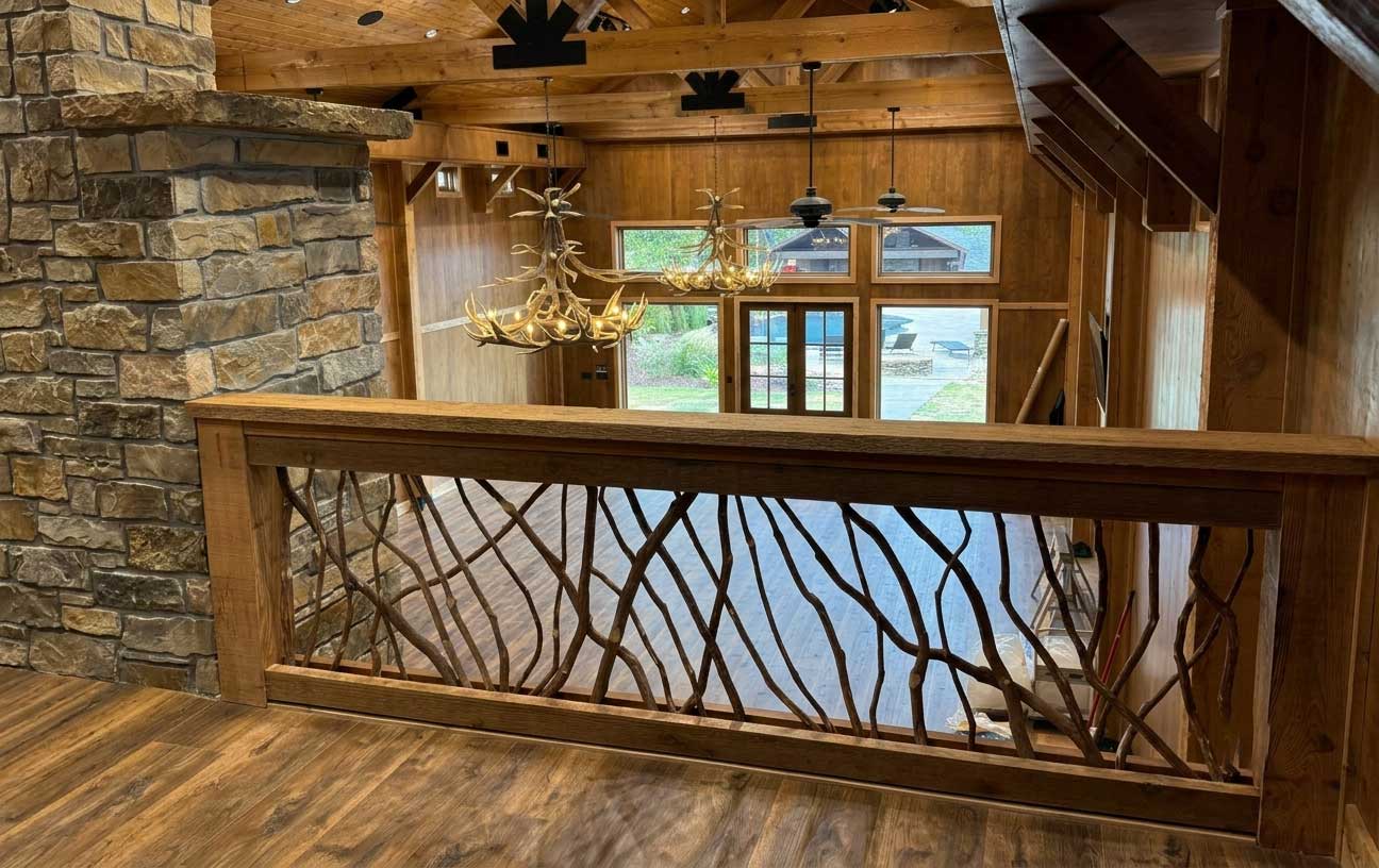 Rustic wooden interior with exposed beams, stone fireplace, antler chandelier, and decorative railing.