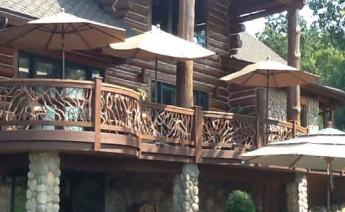 A product photo showing a backed up view of a deck with cobblestone pillars, overlooking a spacious backyard patio with chairs and shading.