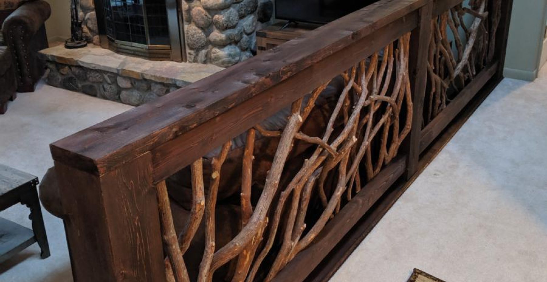 A stylish living room divider featuring a branch railing made of dark painted wood and natural laurel branches, enhancing the rustic decor.