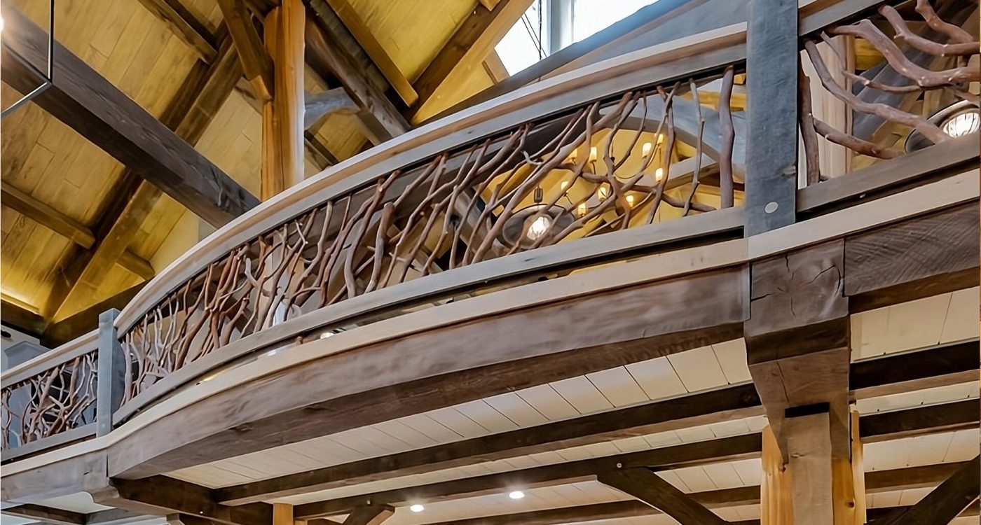 Curved wooden loft balcony with intricate handcrafted woven branch railing inside a spacious log home with high vaulted ceilings and exposed beams.