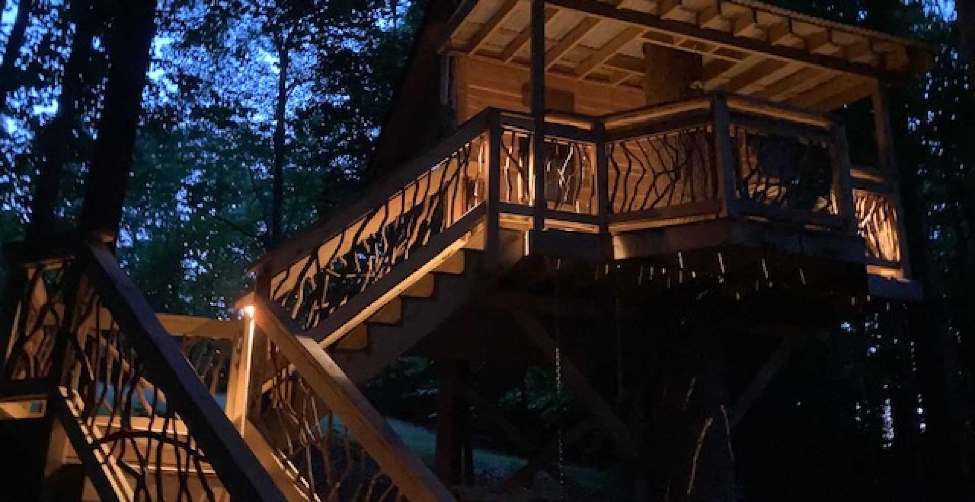 Custom treehouse featuring mountain laurel handrails, elegantly illuminated at nighttime, creating a magical outdoor atmosphere.