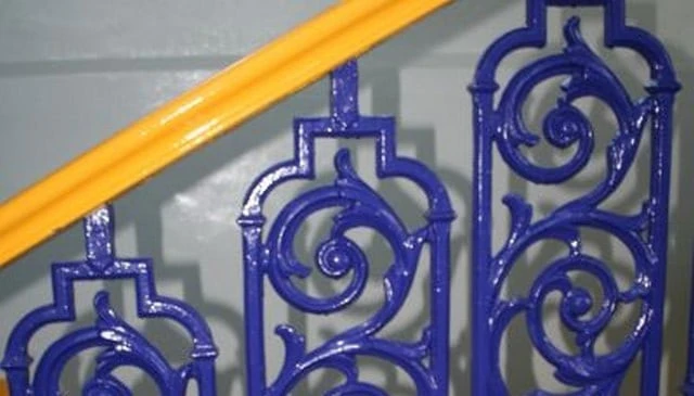 A stair railing design showcasing repeating vine and circle motif balusters in blue with a bright yellow top banister, exemplifying vibrant stair railing designs.