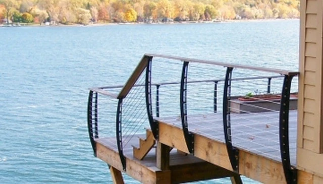A deck overlooking a lake showcasing arched metal newel posts mounted to the deck framing with a wood cap, exemplifying stylish deck railing designs.
