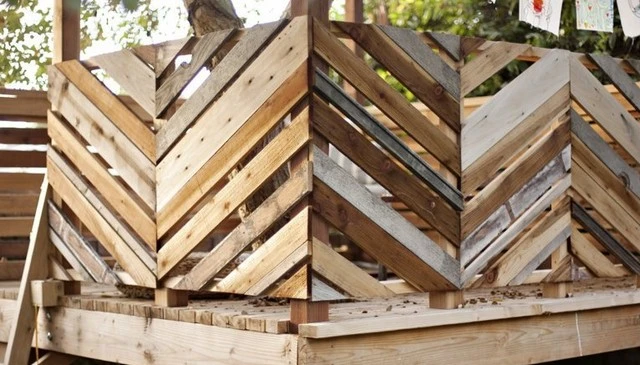 A playful wooden porch railing featuring varied widths and textures, highlighting inverted delta shapes around a tree canopy.