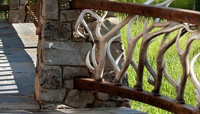 Elk antler railing featuring dry-stacked stone columns and curved cedar 4x4s with antlers sprouting from the bottom, showcasing a unique design.