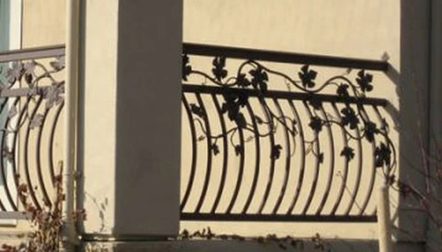 Metal balusters with an arc design showcasing a solid top rail and decorative grape vine and leaves, exemplifying an artistic railing aesthetic in outdoor design.
