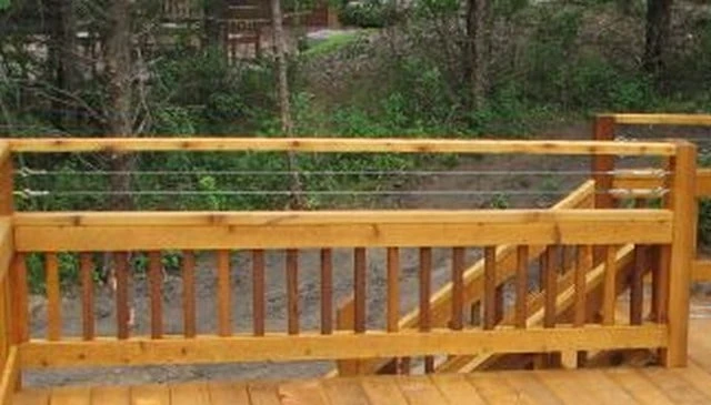 A unique combination of horizontal cable railing above vertical 2x2 pickets showcasing metal and wood elements on a forest deck, exemplifying modern deck railing designs.