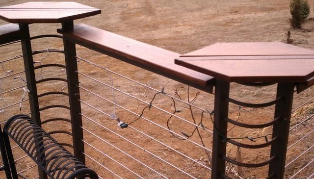 A deck remodel idea showcasing cable railing with formed metal radius corners and a wood 1x6 top, featuring taller posts with small tables, exemplifying modern deck railing designs.