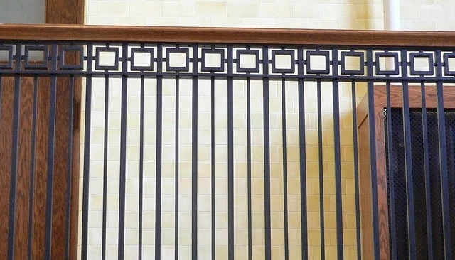 Craftsman style railing in a courthouse showcasing black metal balusters of alternating widths topped with smaller squares and a dark stained wood cap exemplifying sophisticated design.