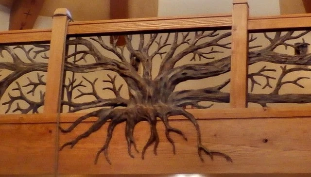 A forged bronze metal tree art showcasing a stunning balcony design with limbs stretching across walls from the floor beam exemplifying artistic deck railing designs.