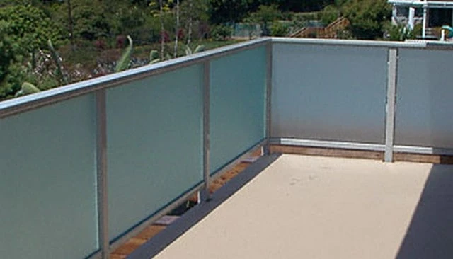 A frosted glass patio handrail providing a privacy effect while allowing light transmission, framed by sturdy metal posts and rails.
