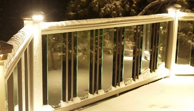 A snowy deck railing design with reflective post lights on white rails, 6-inch glass balusters, and diamond-style 2x2 pickets, creating a winter wonderland aesthetic.