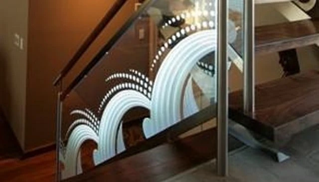 Etched glass panels with an abstract design mimicking a bouncing ball splashing, enhancing the aesthetic of the stair railing.