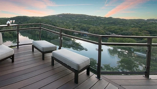 A glass panel guardrail featuring a continuous metal top rail, framed sections overlooking water and a beautiful sunset, enhancing the outdoor experience.