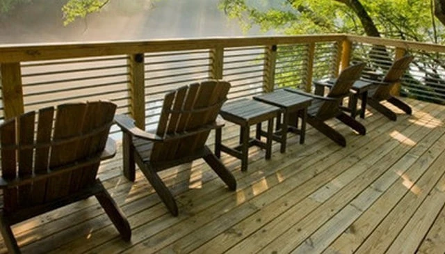 A simple deck railing design with horizontal metal pipes connecting pressure treated 4x4 posts and a wood handrail, providing a stylish barrier overlooking water.