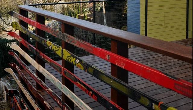 A creative porch deck railing design showcasing horizontally arranged cross country skis complemented by horizontal strung cable railing, adding a unique touch to outdoor spaces.