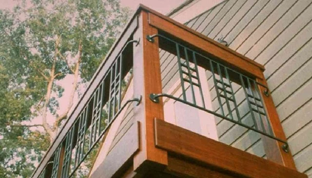 An Ipe wood deck handrail design with enclosed metal sections and craftsman motifs on projecting metal pipes mounted to sturdy posts, combining elegance and functionality.