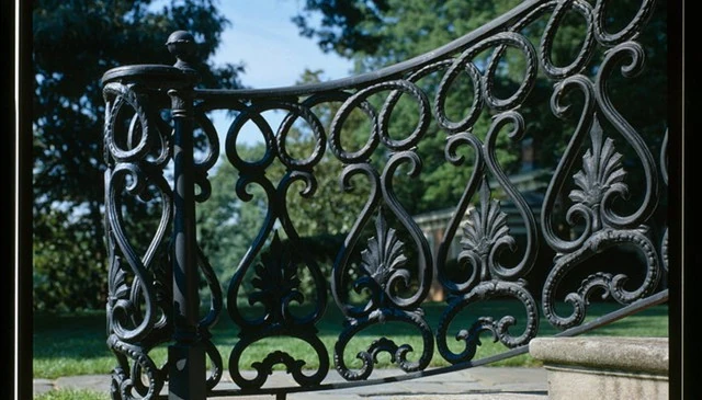 A Grecian urn style iron railing showcasing spade and trident figures topped with coiling metal rope and an open volute design, adding classical elegance to outdoor spaces.