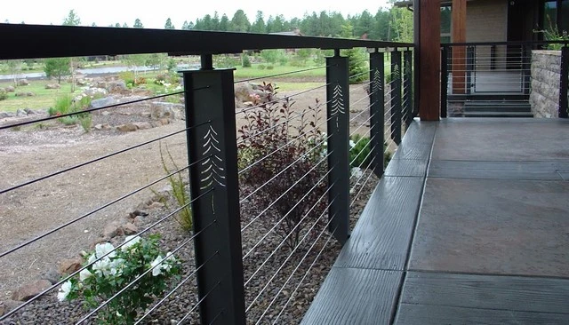 A Keuka Studios Tokyo style cable railing featuring I-beam style posts with pine tree shapes cut out, creating a unique and artistic design for outdoor spaces.