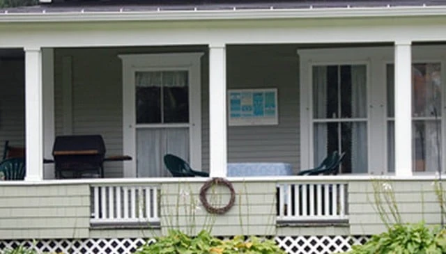 A contemporary porch design featuring a short knee wall railing with vertical 2x2 balusters, complemented by a grill ready for summer gatherings.