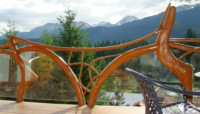 A log and branch handrail design with a curved cut glass inset among natural shapes, providing stunning views and enhancing the aesthetic of outdoor spaces.