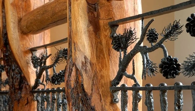A knotty pine post railing featuring large diameter posts with 4-inch log top rails and metal branch pickets adorned with a pine branch and pinecone motif, showcasing innovative deck railing designs.