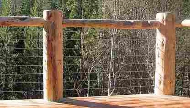 A rustic log railing design with 8-inch diameter posts topped with logs and chicken wire infill, providing safety while allowing for scenic views in innovative deck railing designs.