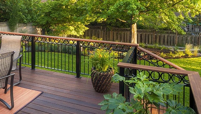 A wooden deck design with black metal posts supporting vertical balustrade sections capped by 4-inch circles and topped with a tropical hardwood rail, showcasing innovative deck railing designs.