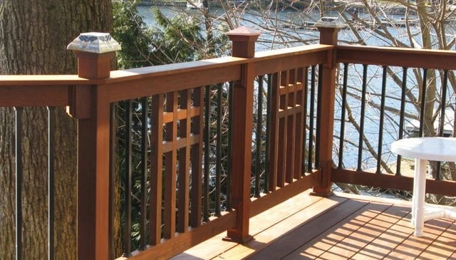 A mission style wood deck railing flanked by metal balusters, with posts capped by alternating glass LED lights and copper caps, showcasing innovative deck railing designs.