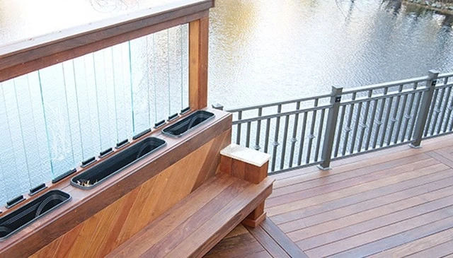 A metal balustrade featuring an Ipe wood deck railing bench, complemented by a glass baluster privacy screen and built-in cooler wells for beverages in innovative deck railing designs.