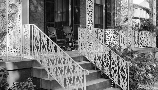 A decorative porch railing and stair handrail showcasing deck railing designs with rightsided up and upside down hearts, complemented by a vine and leaf motif and wrought iron posts.