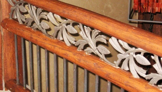 Unique stair railing design featuring three round logs as rails, vertical metal balusters, and a pine cone motif metal insert for distinctive deck railing design.