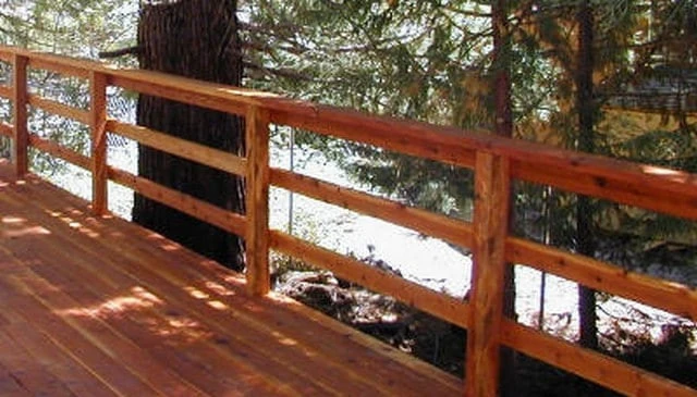 Sparse horizontal deck railing featuring stained cedar boards connected to log posts, creating an open aesthetic for outdoor spaces.