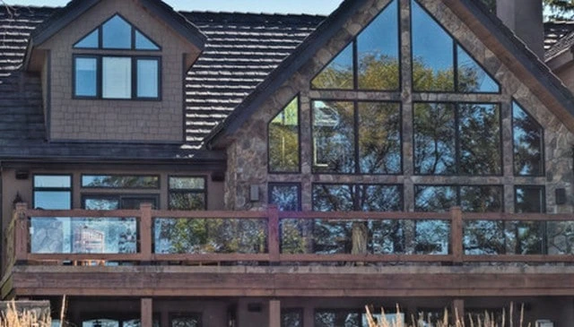 Rustic home design featuring rock siding and a cedar shake roof, complemented by a glass panel handrail and rustic wood posts for unobstructed scenic views.