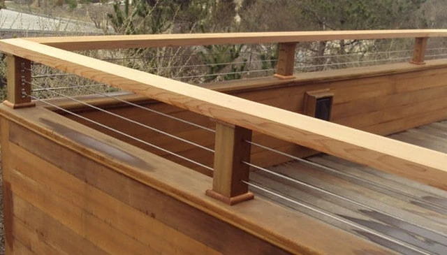Solid wall railing featuring 4x4 posts with copper trims and a 2x4 wood top rail, enhanced by cable strands for stylish deck railing design.